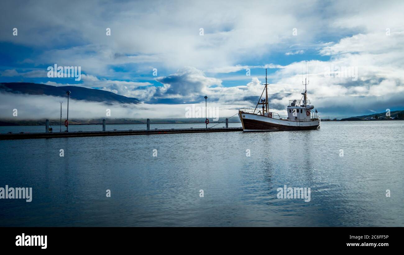 sinister atmosphere at port of akureyri in iceland with a lonely fishing boat waiting in the calm before the polar storm that is coming from mountains Stock Photo