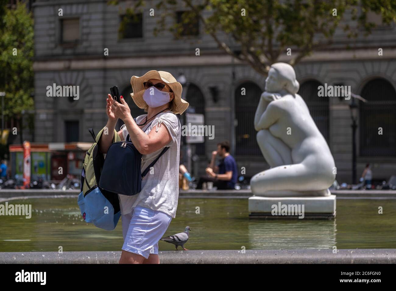 A person taking a selfie next to the sculpture La Diosa by the sculptor Josep Clarà i Ayats in Plaza Catalunya while wearing a face mask as a precaution against the spread of the coronavirus during the pandemic.Catalonia will fine whoever does not wear a sanitary mask in public space with 100 euros, as a measure due to the Covid-19 outbreak. Stock Photo