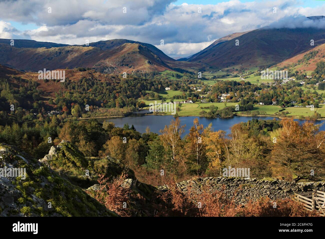 Grasmere in the foreground and upland fells of Helvellyn range in the background with trees coloured golden brown and yellow of the autumn season Stock Photo