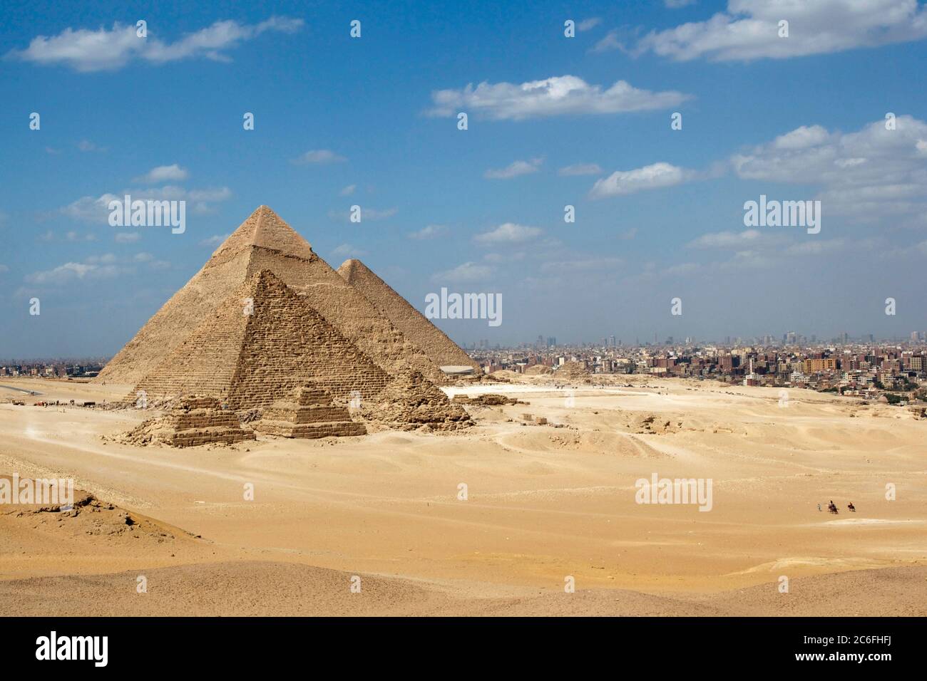 Great Pyramids of Giza set against a bright blue sky and golden yellow desert sands but with the encroaching city of Cairo in the background Stock Photo