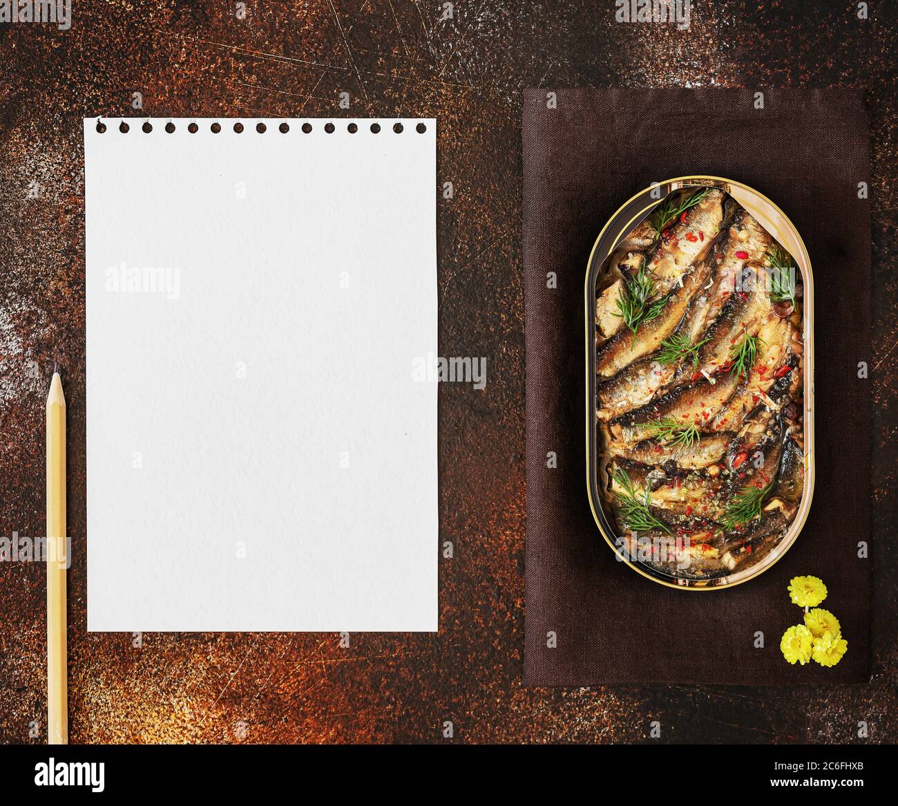 Open tin of Baltic sprats in oil with spices with a sheet of white writing paper and pencil on an old brown background Stock Photo