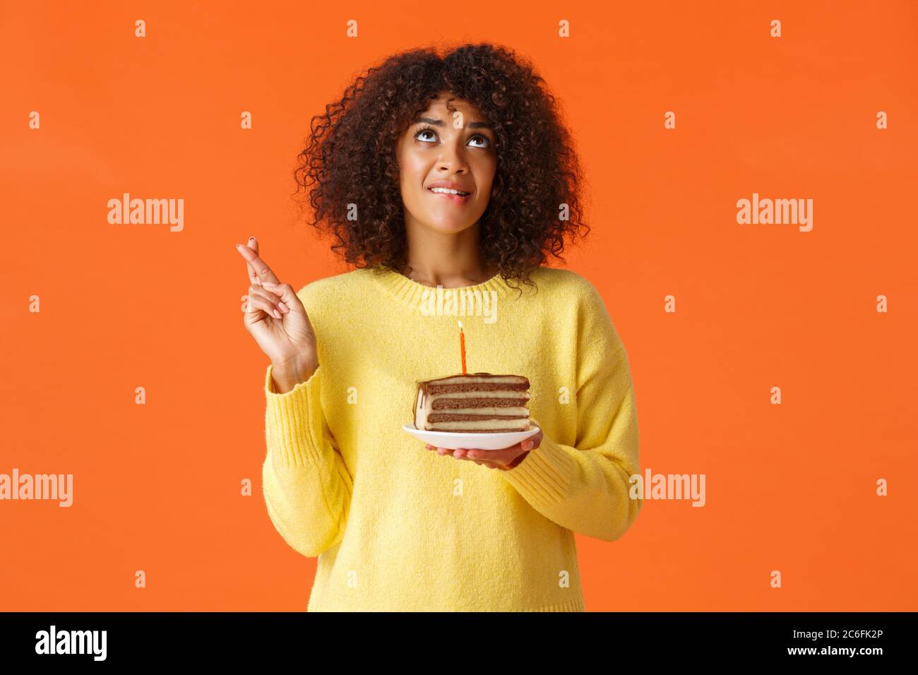 Waist-up portrait hopeful cute dreamy, birthday girl with afro haircut, biting lip and desire wish come true, look up sky praying, cross fingers good Stock Photo