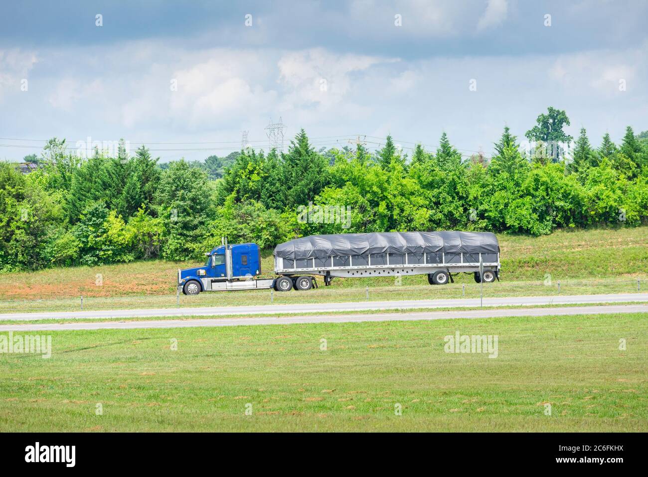 Horizontal shot of a blue 18-wheeler with a covered bed traveling down a Tennessee highway. Stock Photo