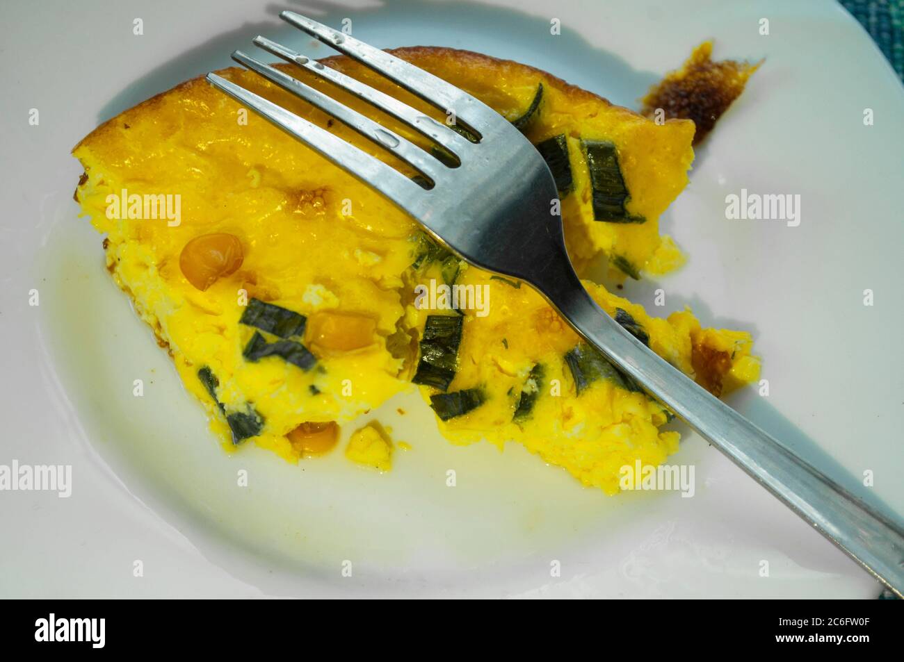On a white plate portion yellow omelet with greens and corn. Fork on the right side Stock Photo