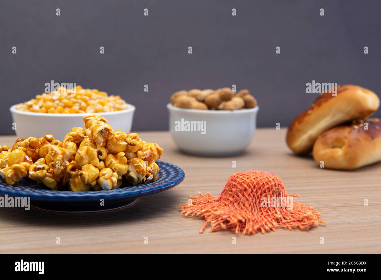 Close up of typical June Party foods on a wooden table: Popcorn, cornmeal cake, corn kernels, peanut pods and small country hats. Copy space. Selectiv Stock Photo