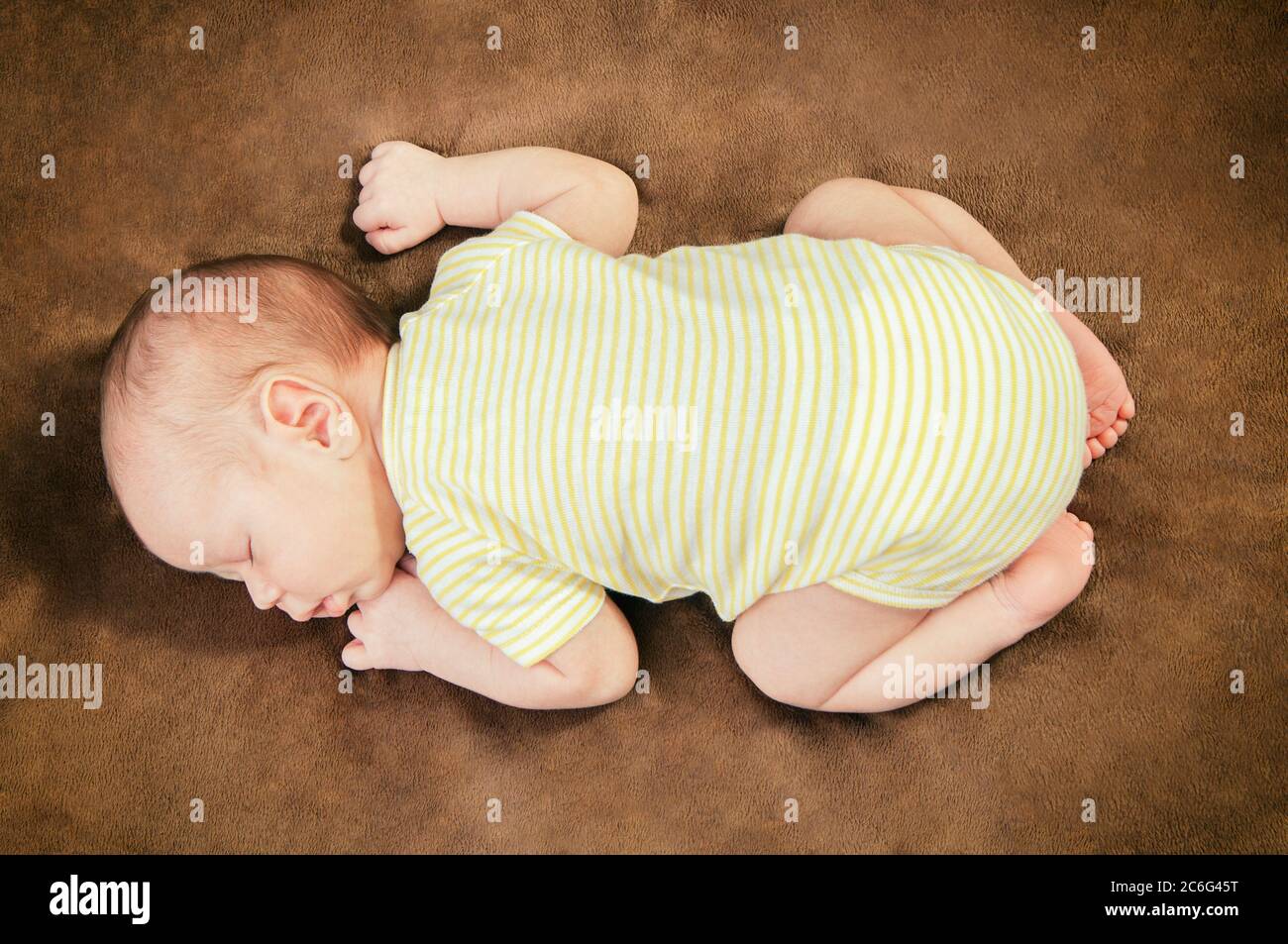 Beautiful newborn baby boy sleeping peacefully on the soft brown blanket Stock Photo