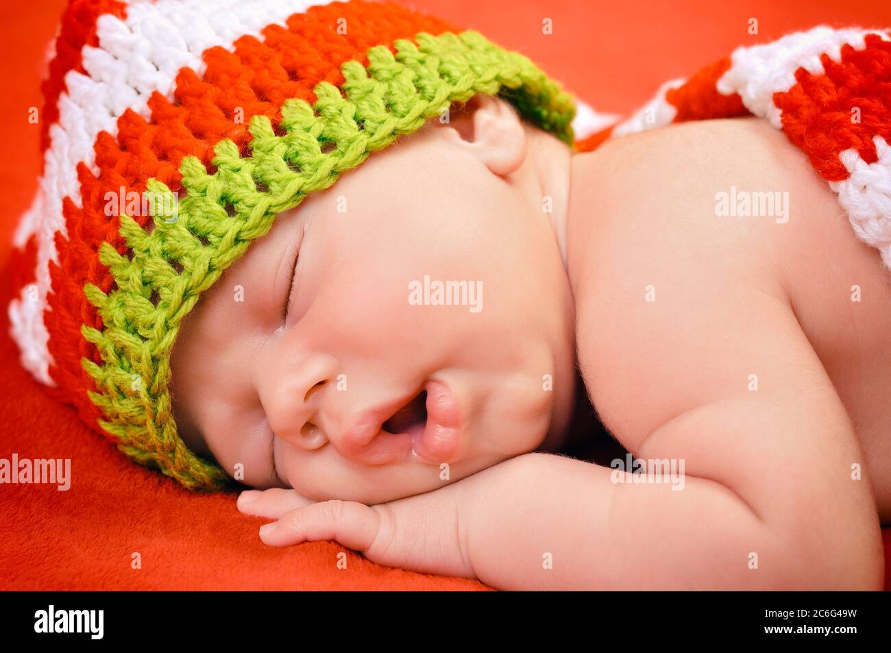 Beautiful newborn baby boy with cute cap sleeping peacefully on the soft red blanket Stock Photo