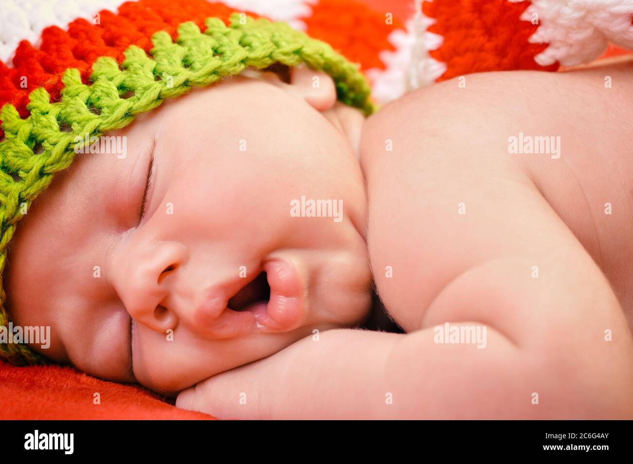 Beautiful newborn baby boy with cute cap sleeping peacefully on the soft red blanket Stock Photo