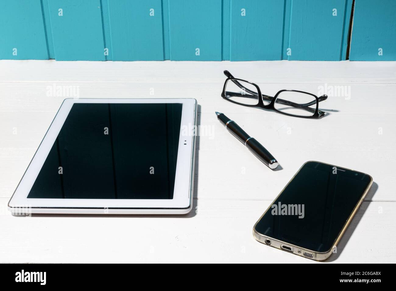 A tablet, a mobile phone and a pair of glasses on a white wooden table Stock Photo