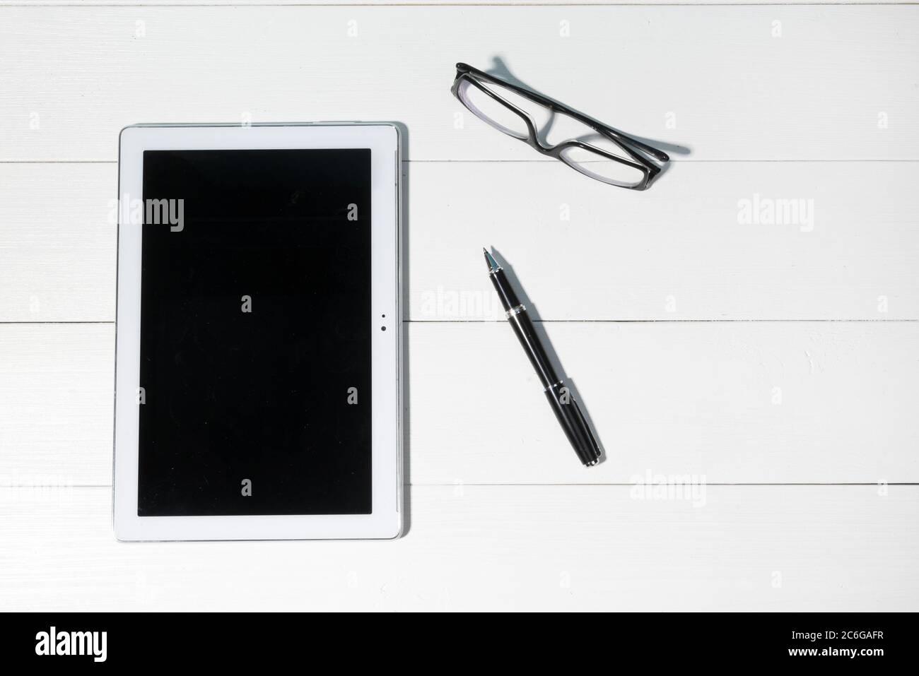 a tablet and a pair of glasses on a white wooden table Stock Photo