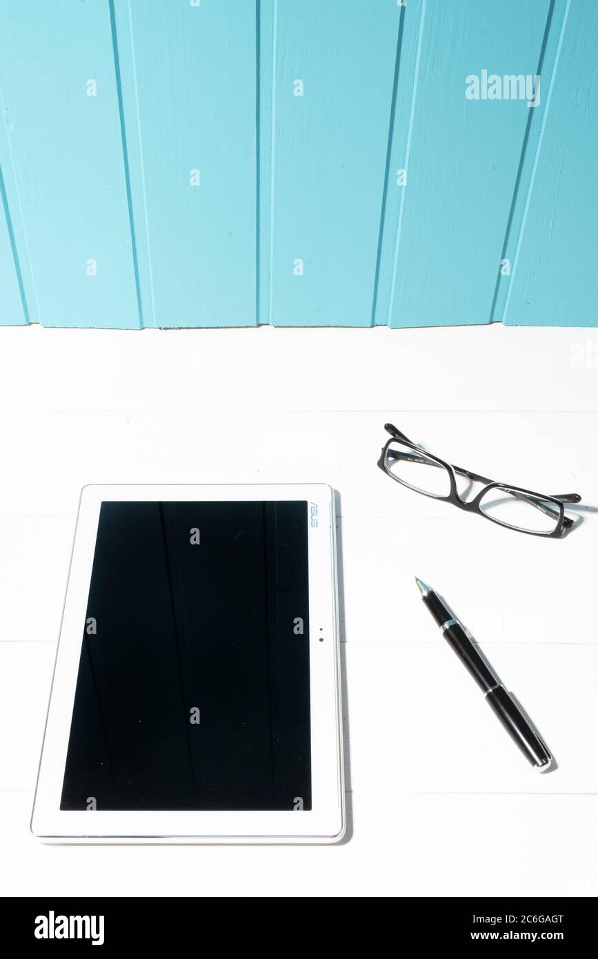 a tablet and a pair of glasses on a white wooden table Stock Photo