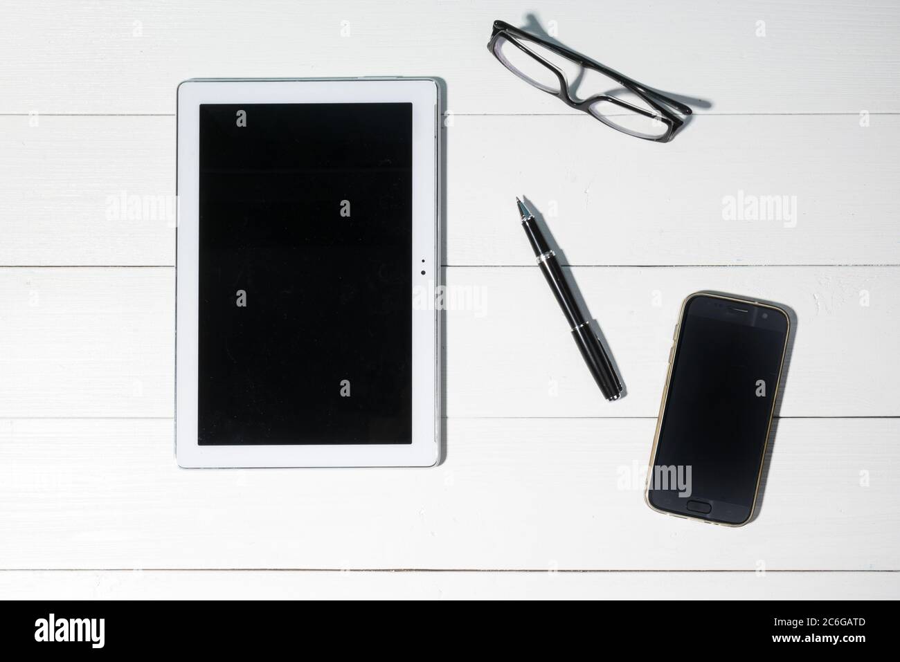 A tablet, a mobile phone and a pair of glasses on a white wooden table Stock Photo