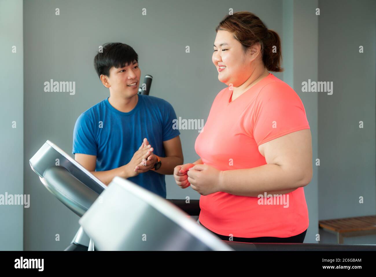 Two Asian trainer man and Overweight woman exercising training on treadmill in gym, trainer looking happy her result during workout. Fat women take ca Stock Photo