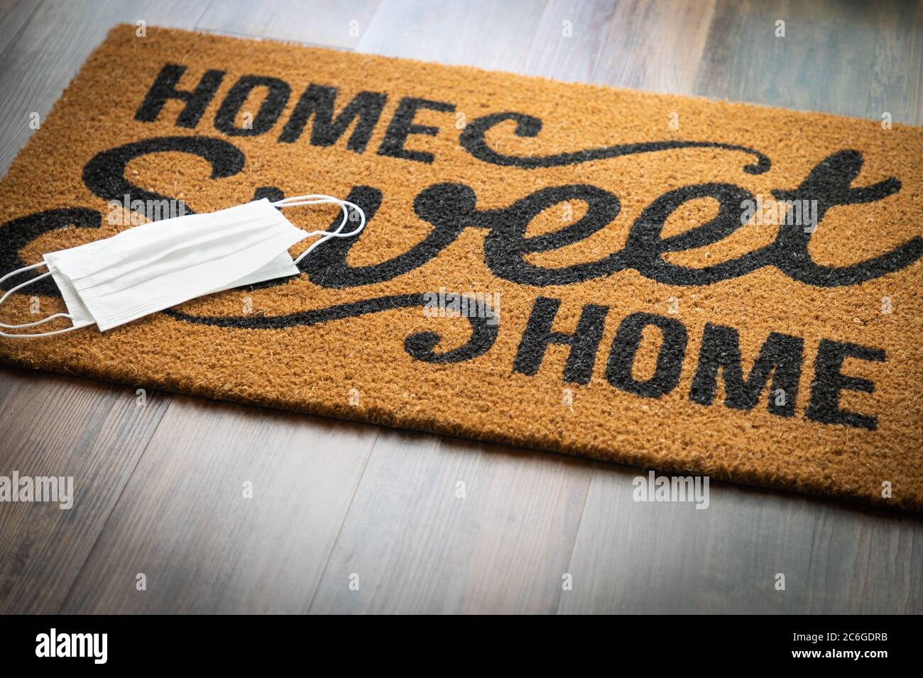 Medical Face Masks Rests on Home Sweet Home Welcome Mat Amidst The Coronavirus Pandemic. Stock Photo