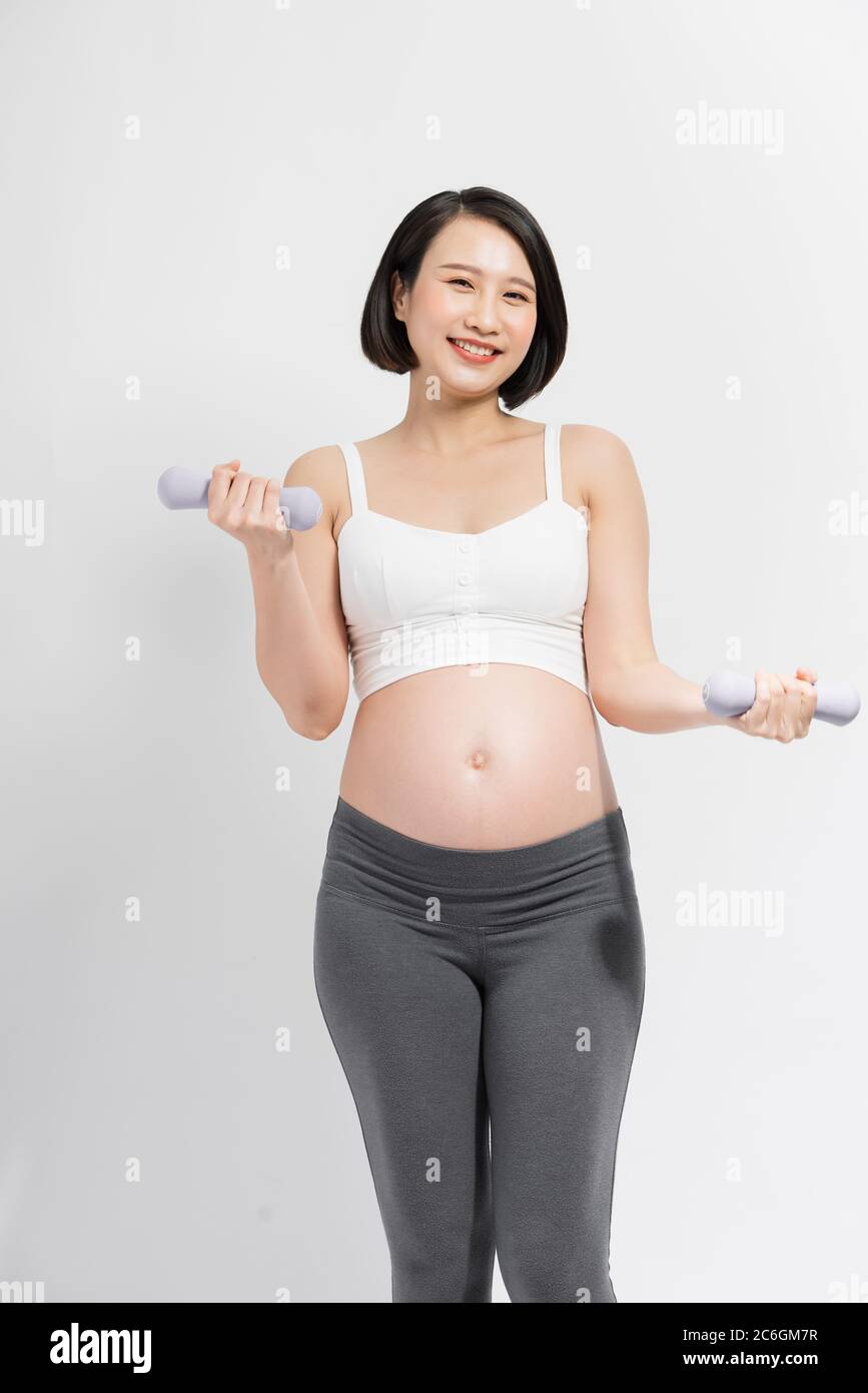Young pregnant woman with beautiful healthy body holding dumbbells Stock Photo