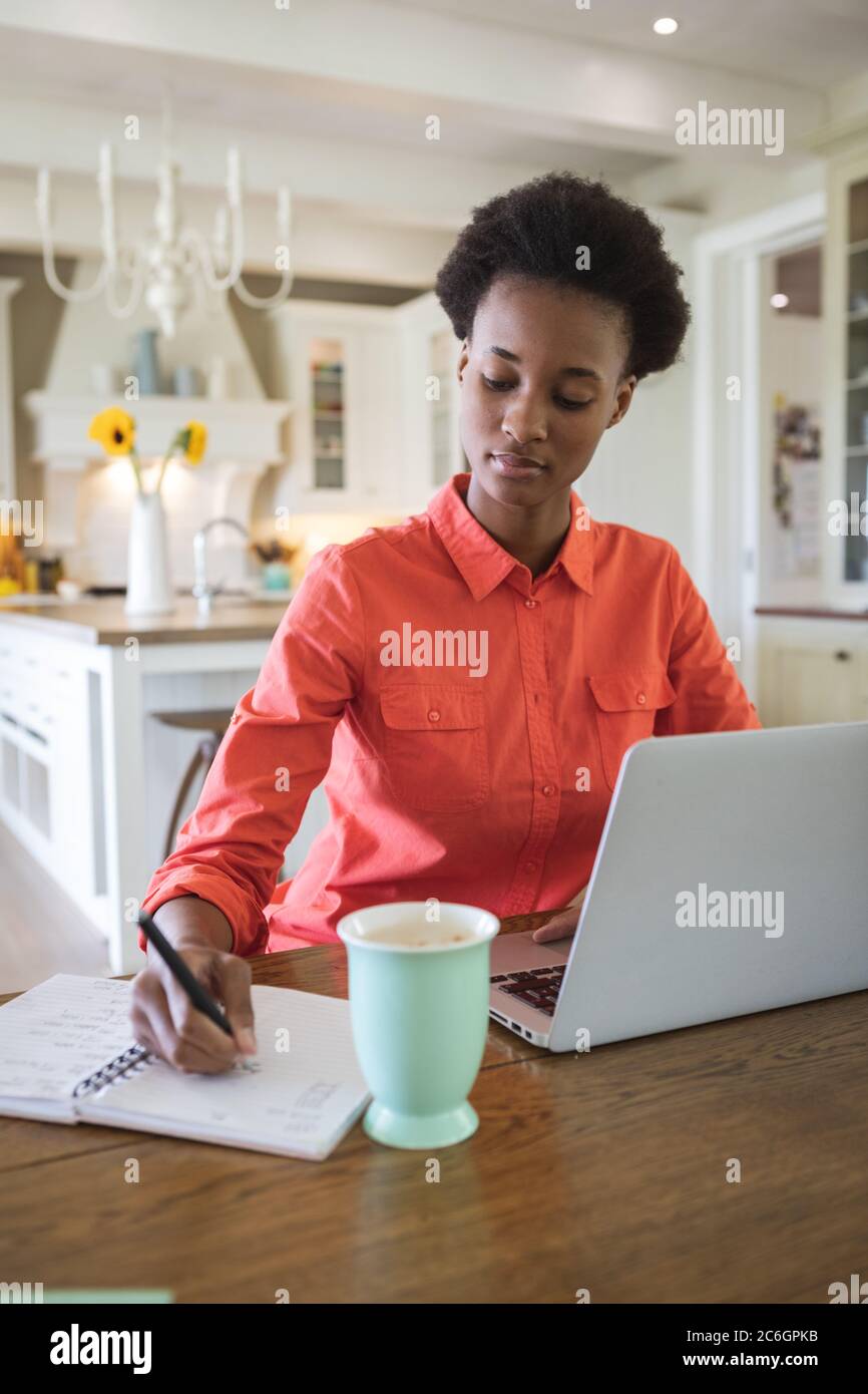 Woman taking notes while using laptop in the kitchen Stock Photo
