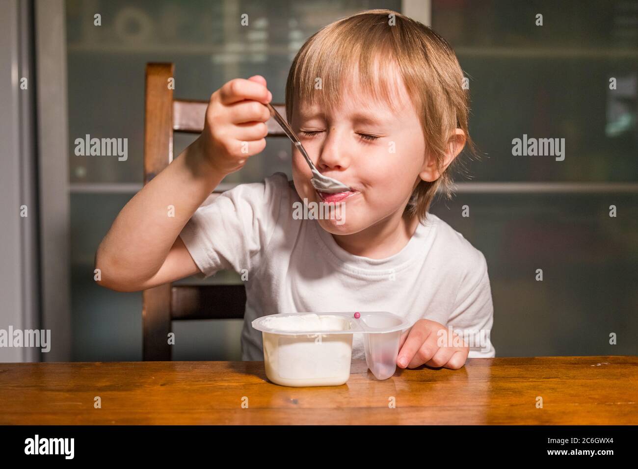 Adorable baby girl eating cottage cheese from spoon, healthy milk snack