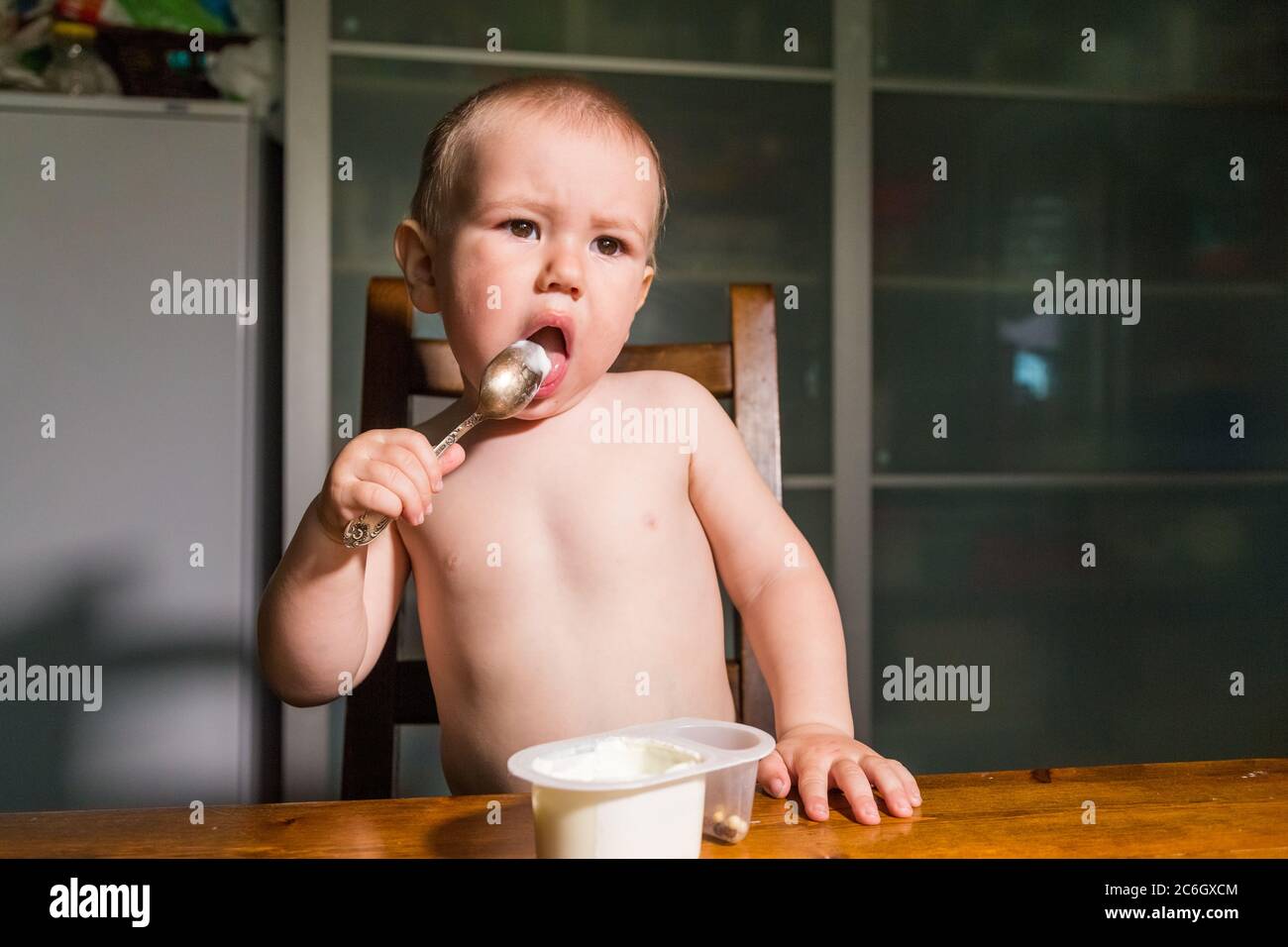 Adorable baby boy eating cottage cheese from spoon, healthy milk snack