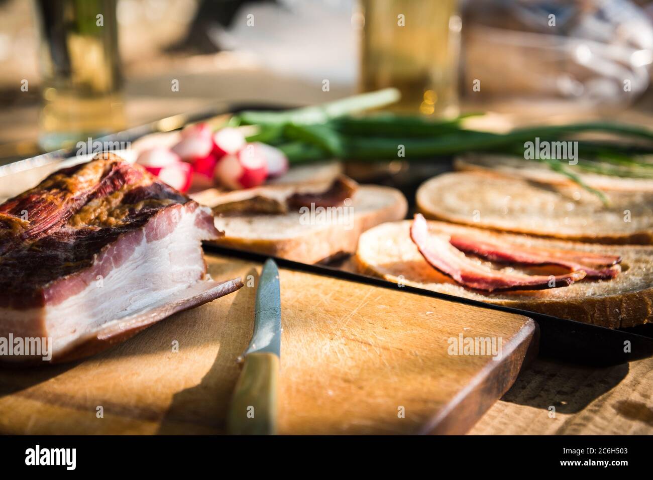 Bacon and knife on a wooden desk. Grilled bacon slice on fatty bread, green onion and fresh radish in the background on a hungarian summer grill party Stock Photo