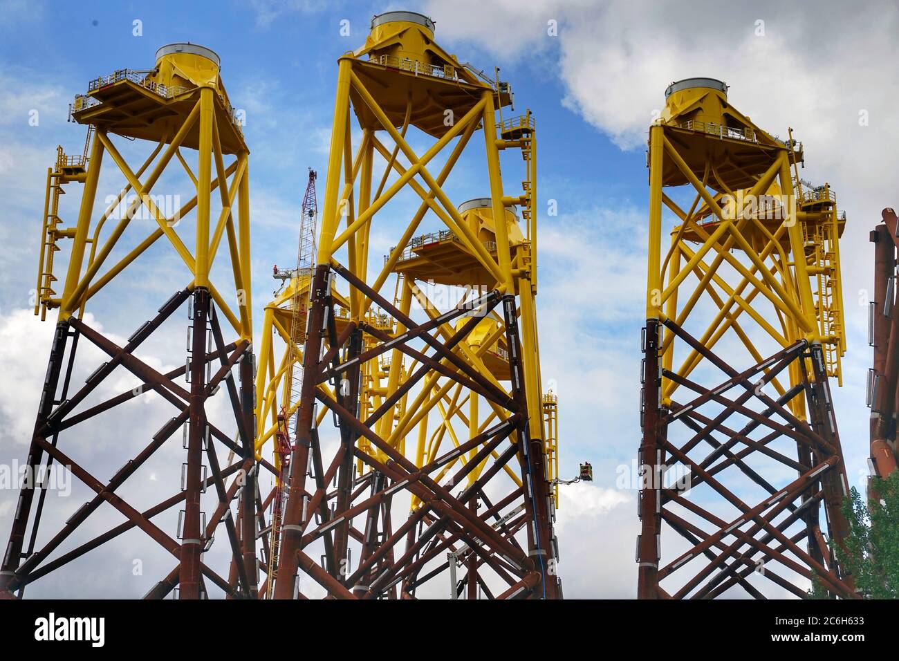 The bases of offshore wind turbines tower over the sky line on the banks of the River Tyne before they are towed out to sea. Stock Photo