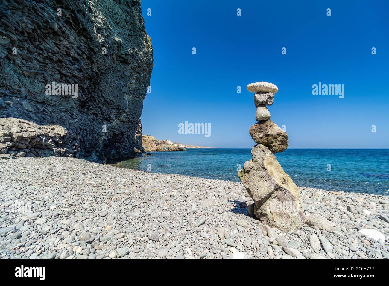Balanced Pebbles Pyramid on the isolated Beach on Sunny Day and Clear Sky. Blue Sea on Background. Selective focus, Bokeh. Zen stones on sea beach Stock Photo