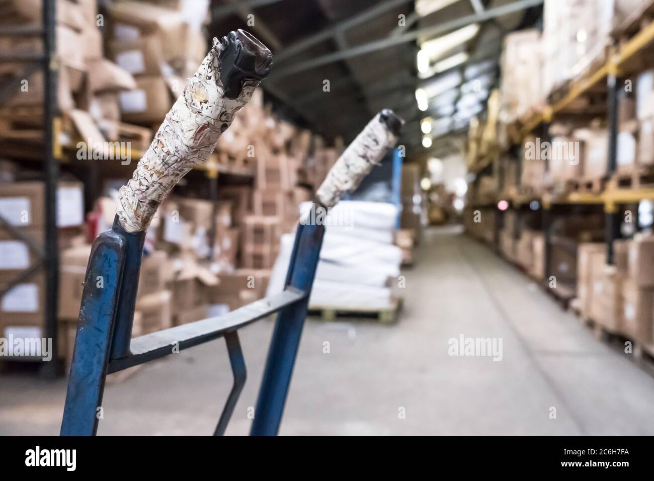 Interior view of a distribution and warehouse facility. Showing detail of a nearby manual pump truck handle, with an out of focus view of the facility. Stock Photo
