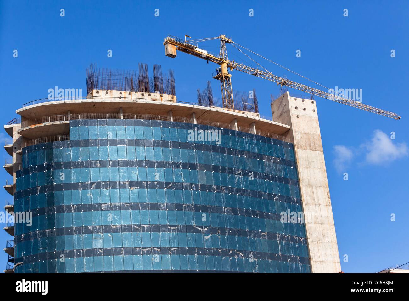 New building construction halfway about eight floors steel scaffolding and cranes with outer window glass panels been installed on site on a clear blu Stock Photo