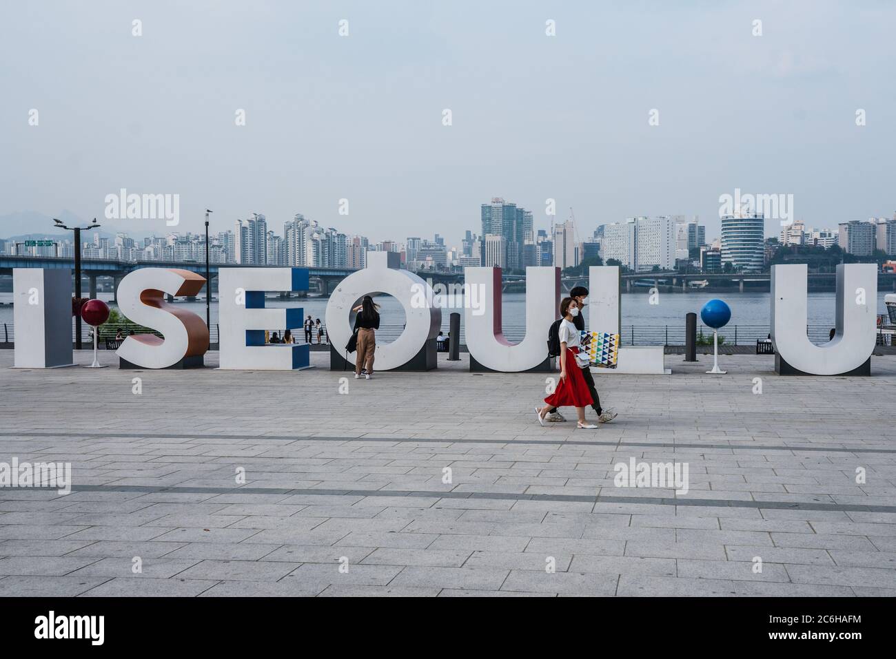 People wearing protective masks walk past 'I Seoul U' board on the riverside.50 new coronavirus cases were confirmed by Korea Centres for Disease Control (KCDC) on 9 July during the Second Wave of the virus. Stock Photo
