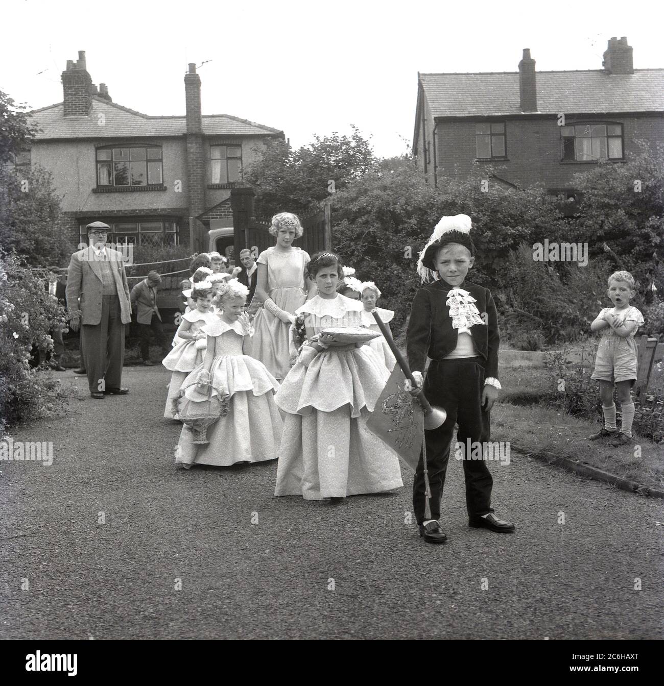 1950s, historical, the Rose Queen, a local teeage girl, with other young girls in their costumes walking in a procession led by a young boy dressed in a regency outfit and carrying a trumpet at Farnworth, Bolton, Lancashire, England, UK. Dating back to the 1880s, the annual Rose Queen festival, held in June, became a major annual event in many towns and villages across the UK, especially in Lancashire, known as the red rose county, following the 1455-87 Wars of the Roses. Stock Photo