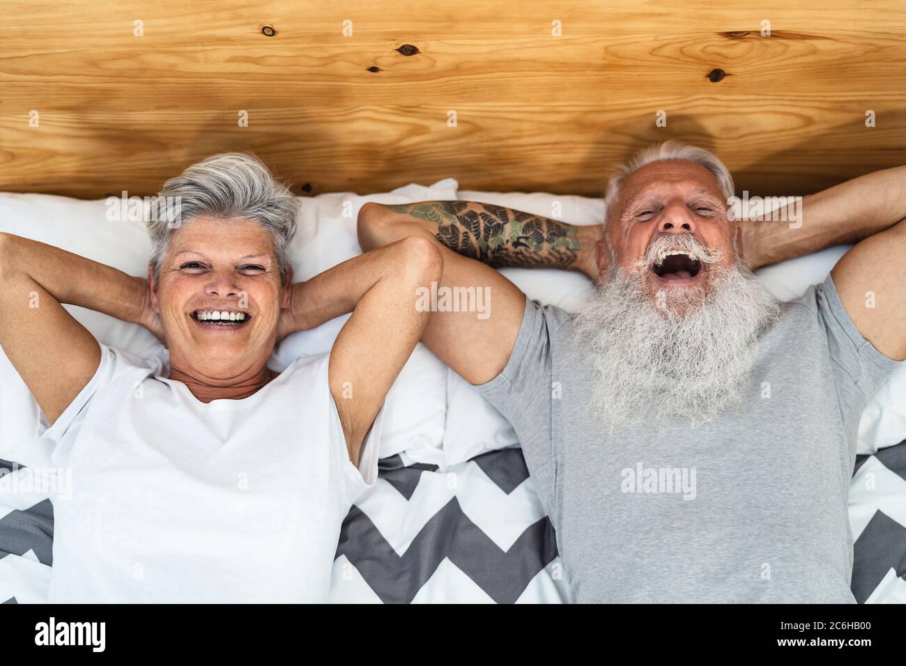 Happy senior couple in bed - Hipster mature people having funny bed time together - Elderly lifestyle and love relationship concept Stock Photo