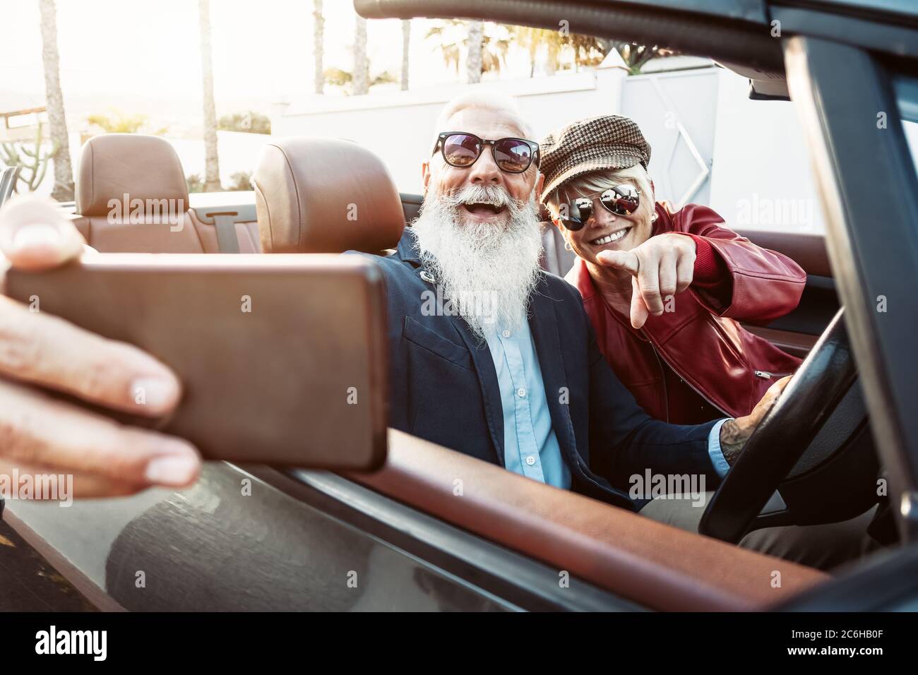 Happy senior couple taking selfie on new convertible car - Mature people having fun in cabriolet together during road trip vacation Stock Photo