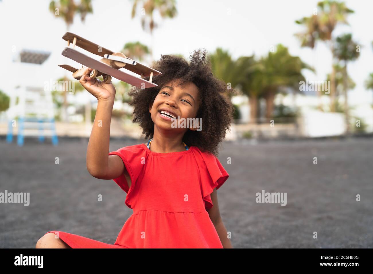 Afro child playing with wood toy airplane on the beach - Little kid having fun during summer holidays - Childhood and travel vacation concept Stock Photo