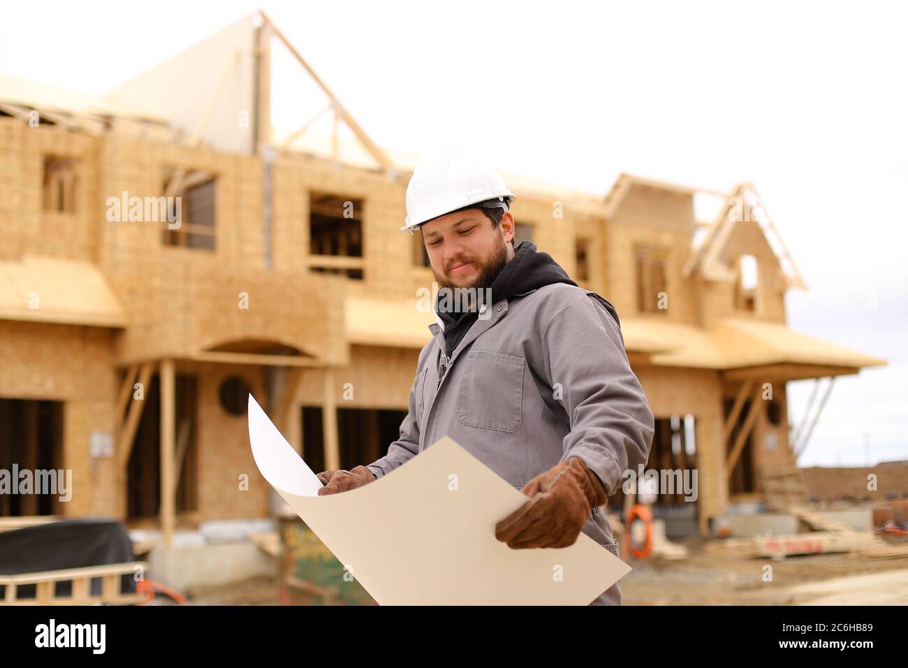 Bearded builder holding architectural drawing plan on paper at construction site. Stock Photo