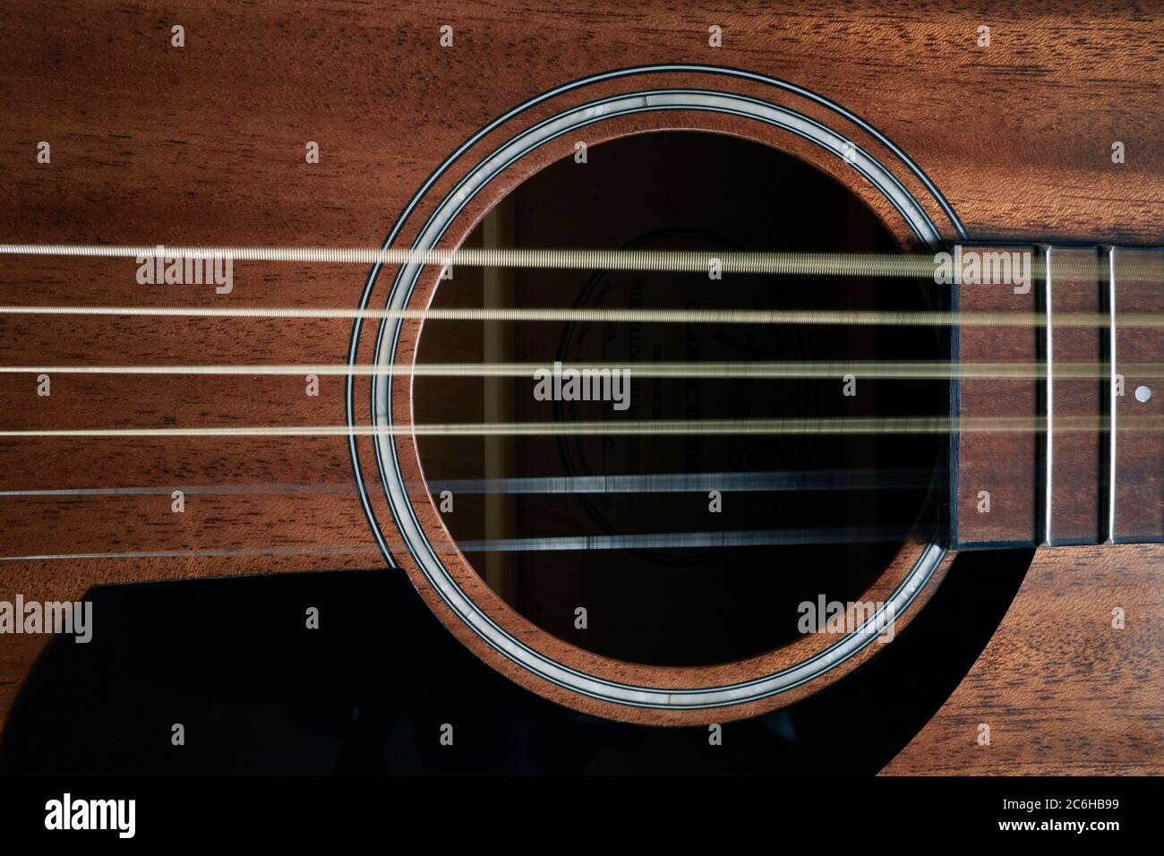 A close up photograph of a Fender acoustic guitar showing the sound hole and part of the fretboard. Guitar strings show movement, wavy guitar strings. Stock Photo
