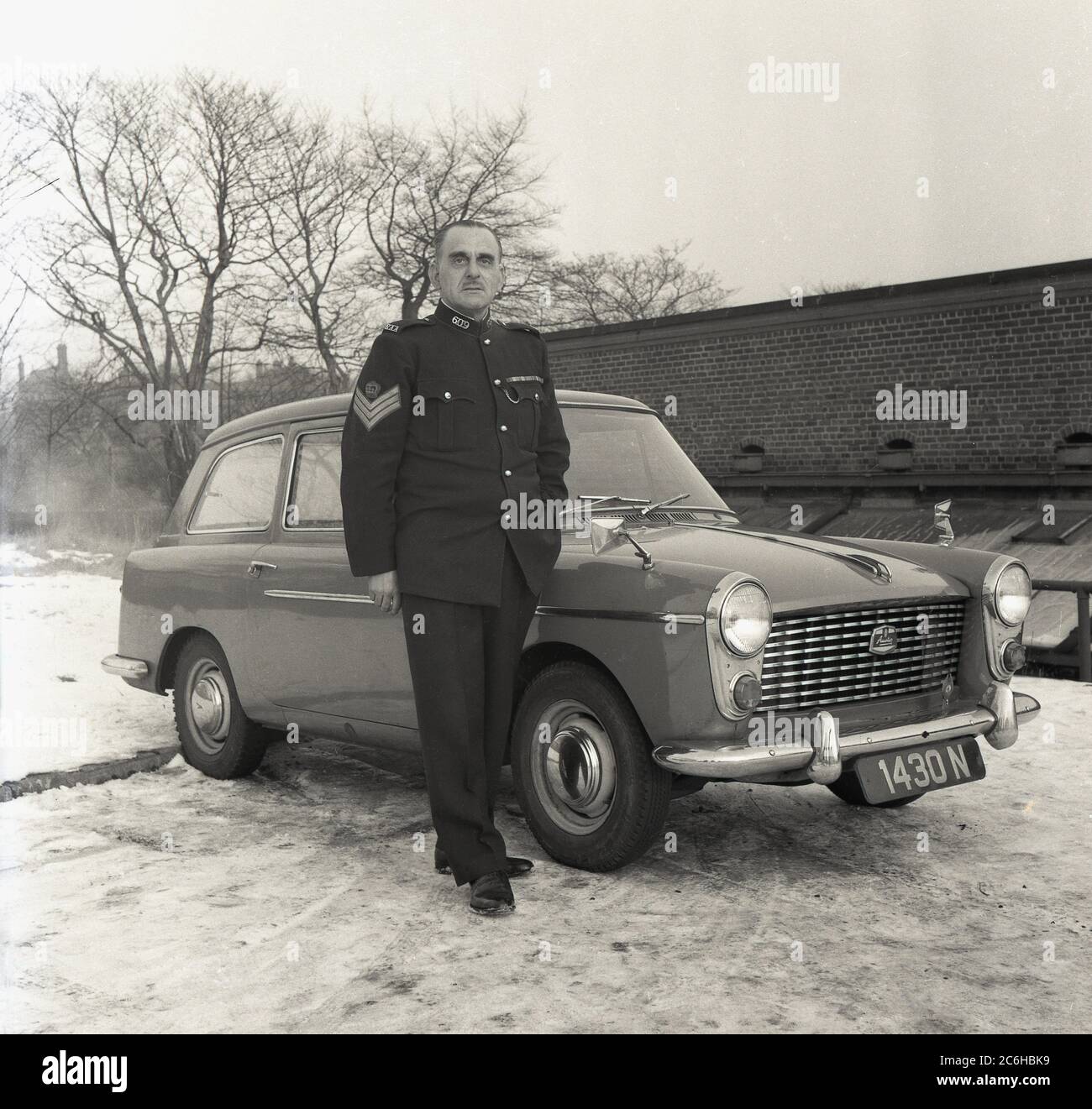 1960s, historial, wintertime and with snow on the ground outside, a Sergeant of the Royal Artillery in his uniform standing for a photo by his Austin A40 car, England, UK. Founded in 1716, the Royal Regiment of Artillery, known as 'The Gunners', is one of two regiments that make up the arttillery arm of the British Army. Stock Photo