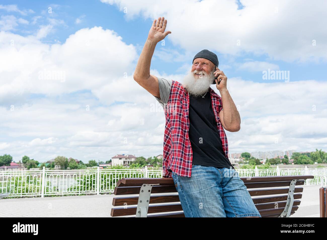 Portrait of elderly bearded gentleman in coat talking on cellphone. He is looking away and smiling Stock Photo