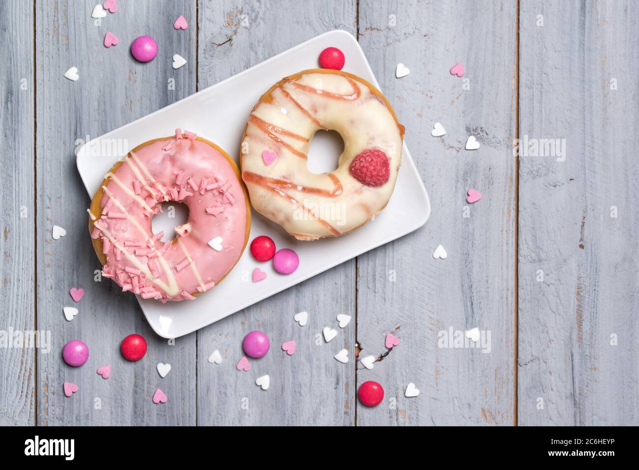 Two donuts on a plate decorated with smarties and sprinkles hearts, wooden background Stock Photo