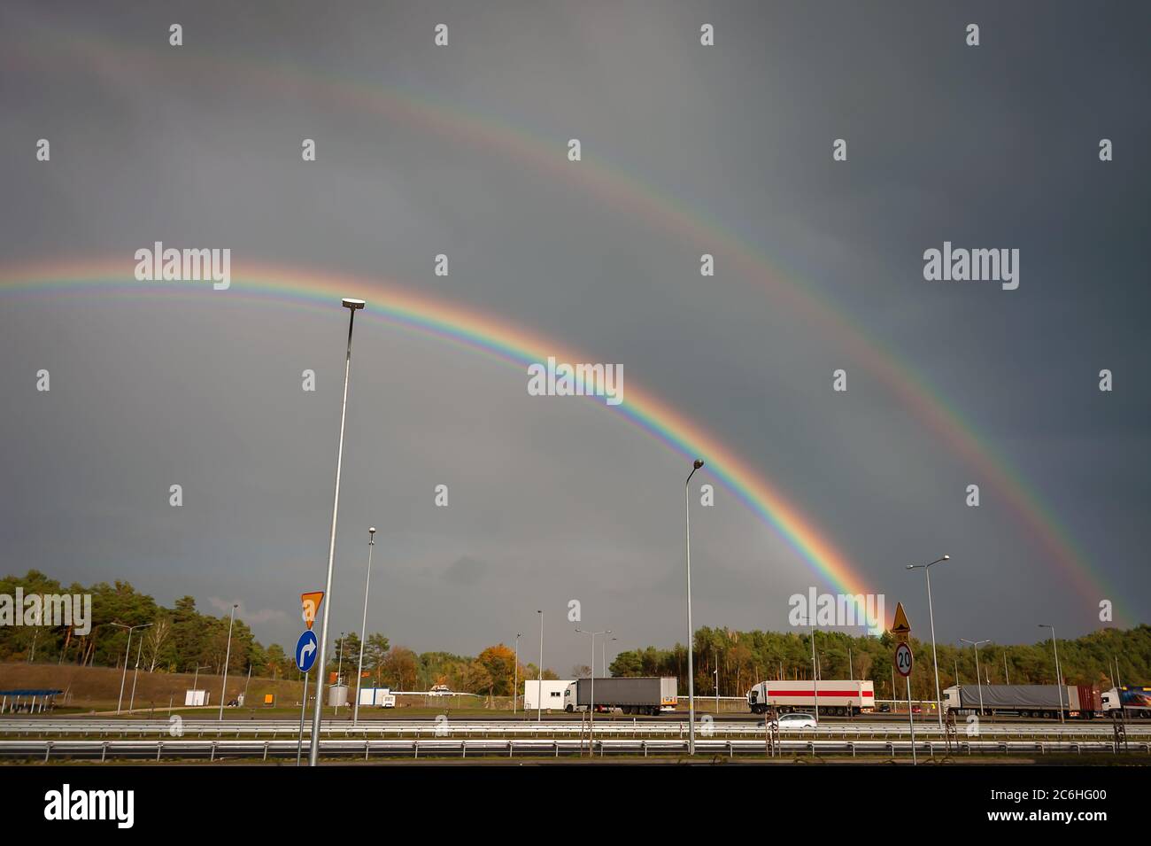 Double rainbow over a motoroway with long haul trucks. Colourful autumn landscape with rainbows in a dark stormy sky Stock Photo