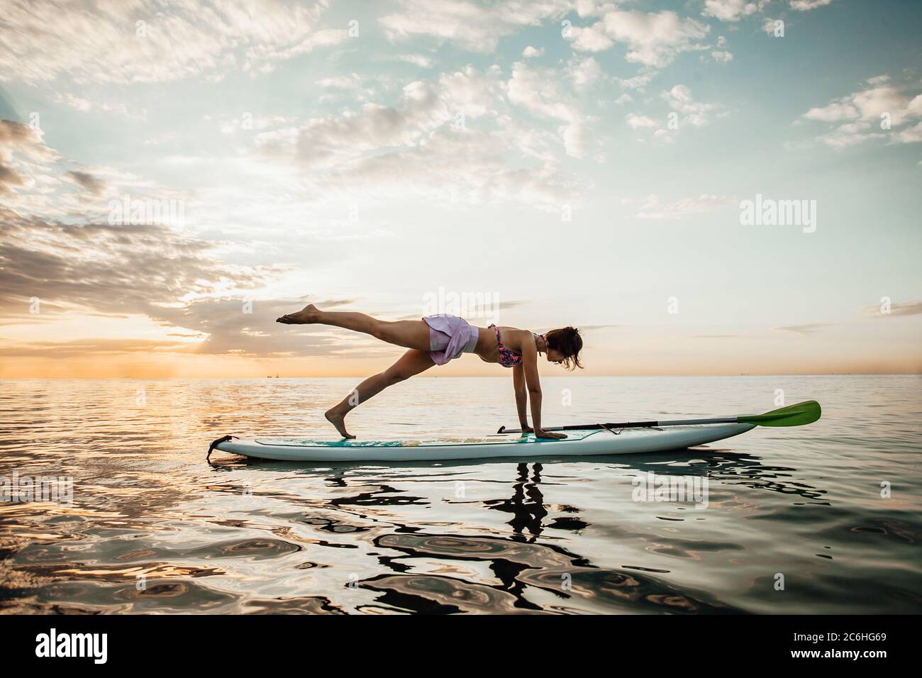 Young woman doing YOGA on a SUP board in the lake at sunrise Stock Photo