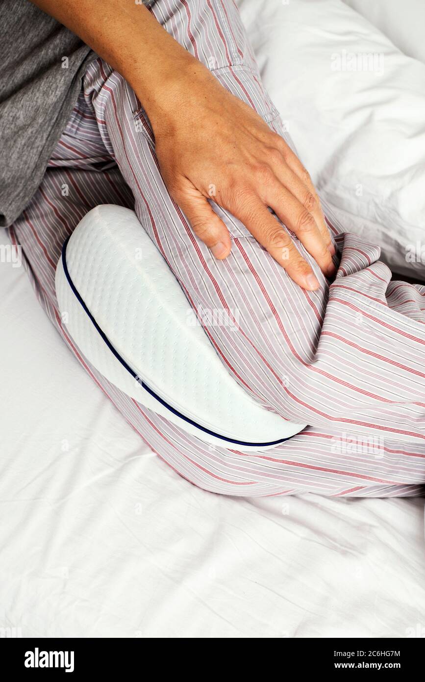 https://c8.alamy.com/comp/2C6HG7M/closeup-of-a-caucasian-man-wearing-striped-pajama-pants-using-an-anatomical-cushion-between-his-legs-while-is-lying-on-a-bed-set-with-white-bedsheet-2C6HG7M.jpg