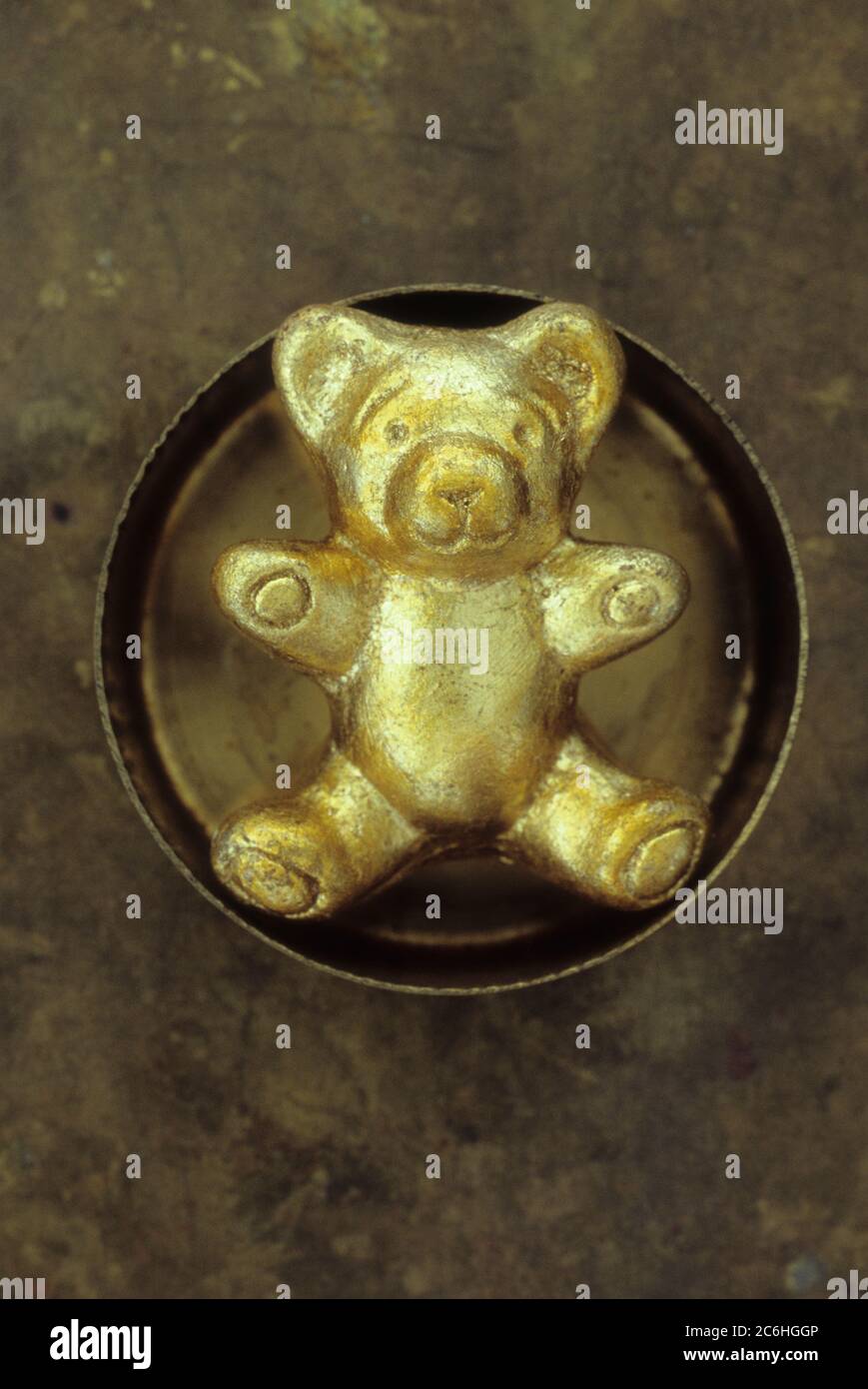 Small model of solid teddy bear painted gold and sitting with arms outstretched in brass dish Stock Photo