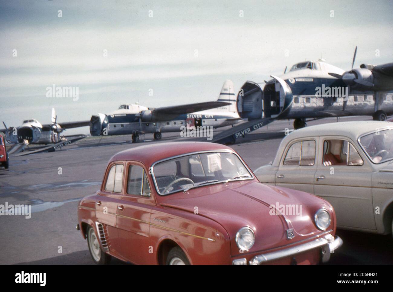 1960. Three Bristol Freighter aircraft of Silver City Airways. Their cargo doors are open and ramps down. Two period motor cars are parked in the foreground, waiting to board the aircraft. Stock Photo
