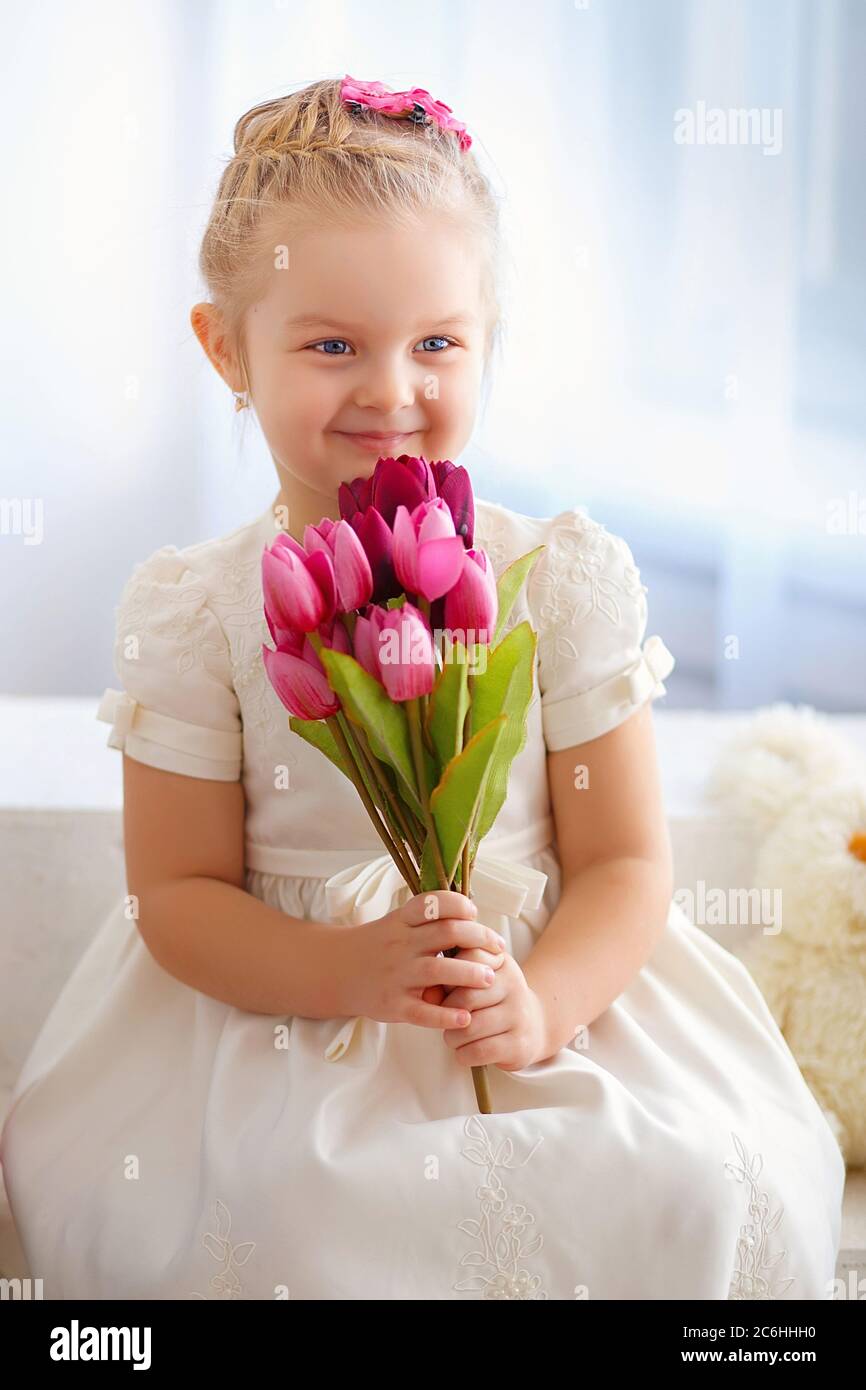 beautiful little girl in a white dress sitting on a windowsill with a ...
