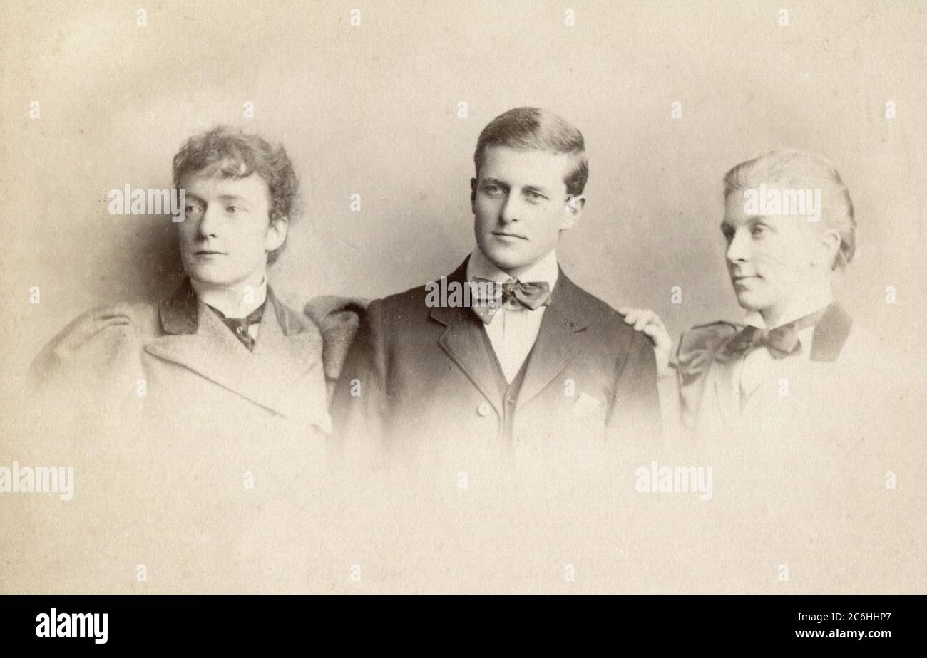 Circa. 1890s. A Victorian portrait photograph of a gentleman with his two sisters. Stock Photo