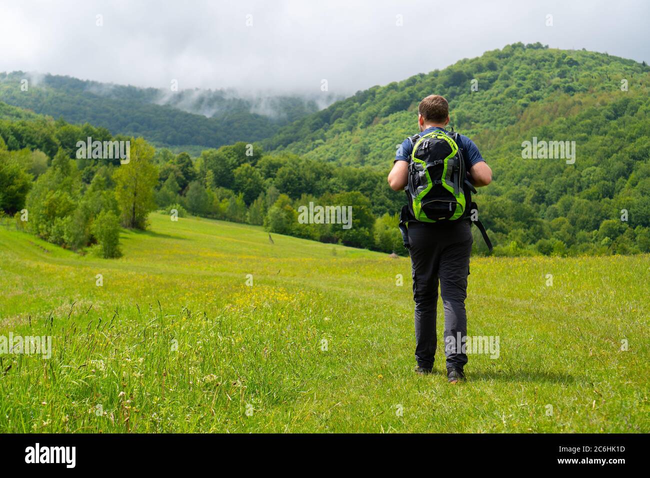 get out of the house and go to the mountains. guy with a green backpack heading the wooded mountains. Carpathians Stock Photo