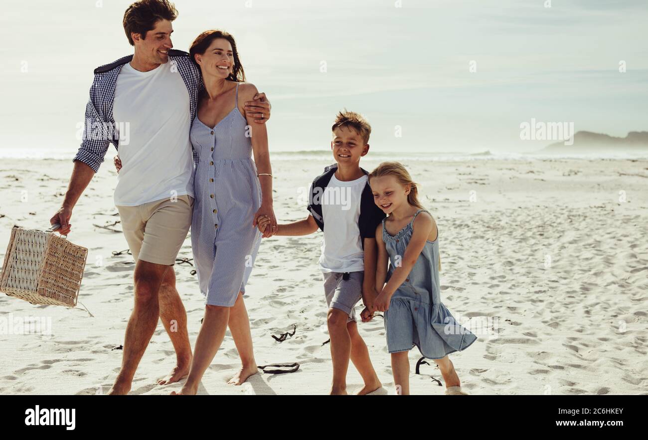 Kids walking with their parent along the beach on summer day. Family of four at beach for a picnic. Stock Photo