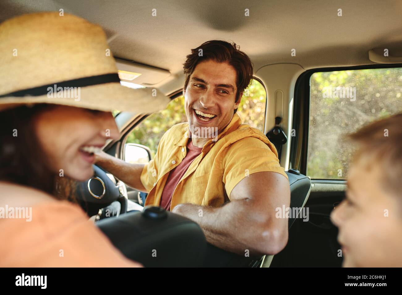 Family going on a holiday in car. Smiling father and mother turns around to their son sitting on the back seat of car. Stock Photo