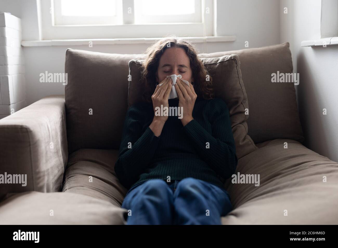 Woman blowing her nose on the couch at home Stock Photo