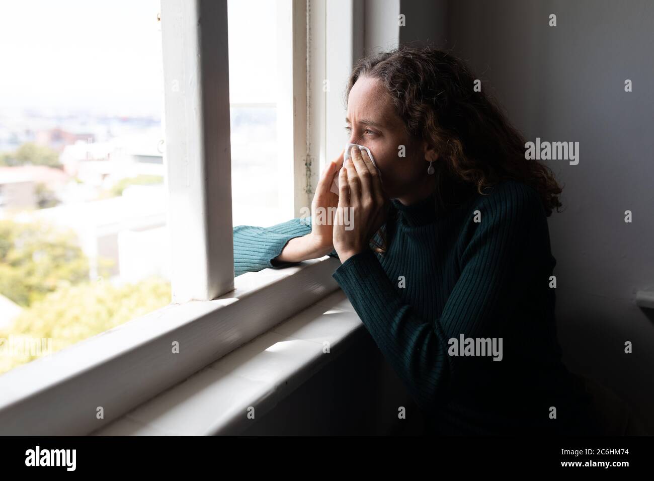 Woman blowing her nose near the window at home Stock Photo