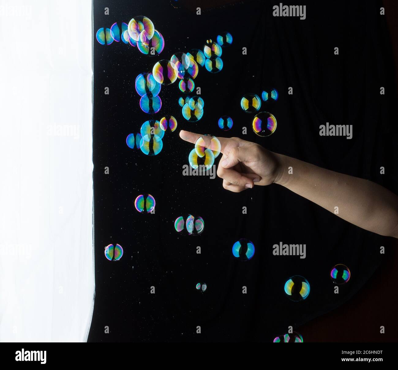 Hand Interacting with Colorful Floating Soap Bubbles. Stock Photo